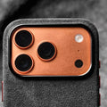 Genuine Italian Alcantara case in black with metal camera ring on an orange iPhone 17 Pro